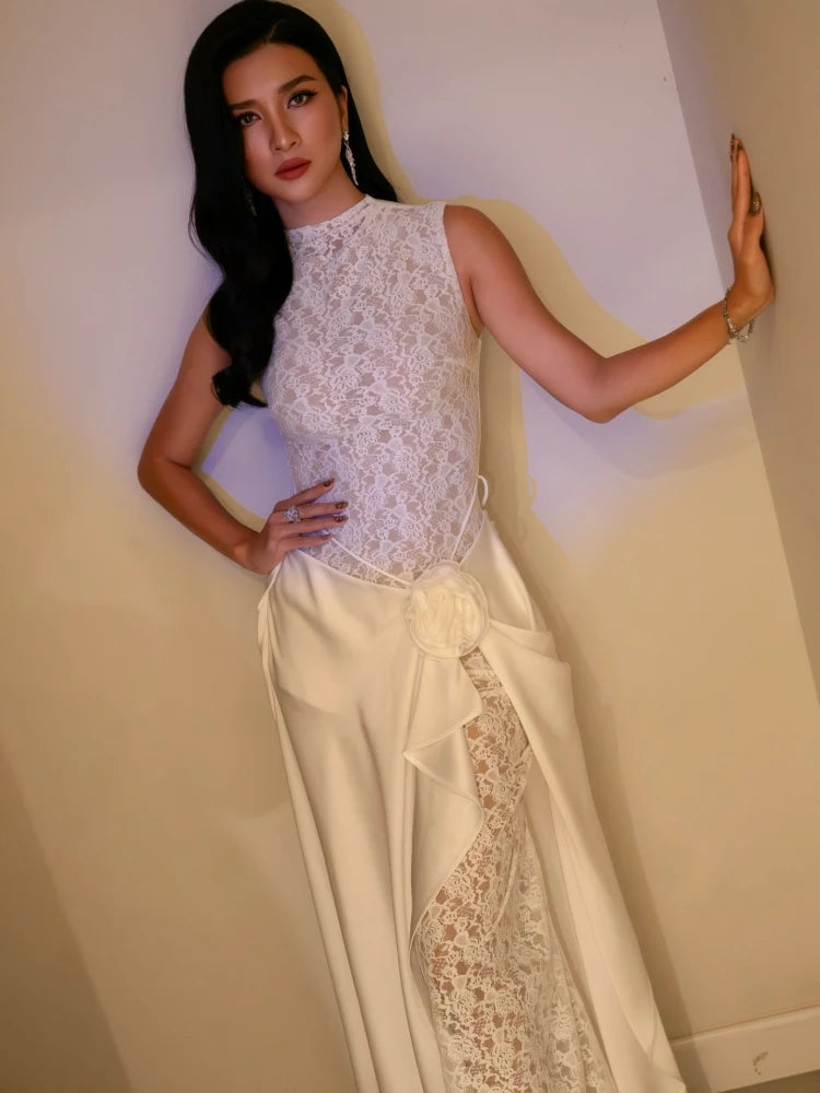 Woman wearing a white lace top and skirt against a plain wall.