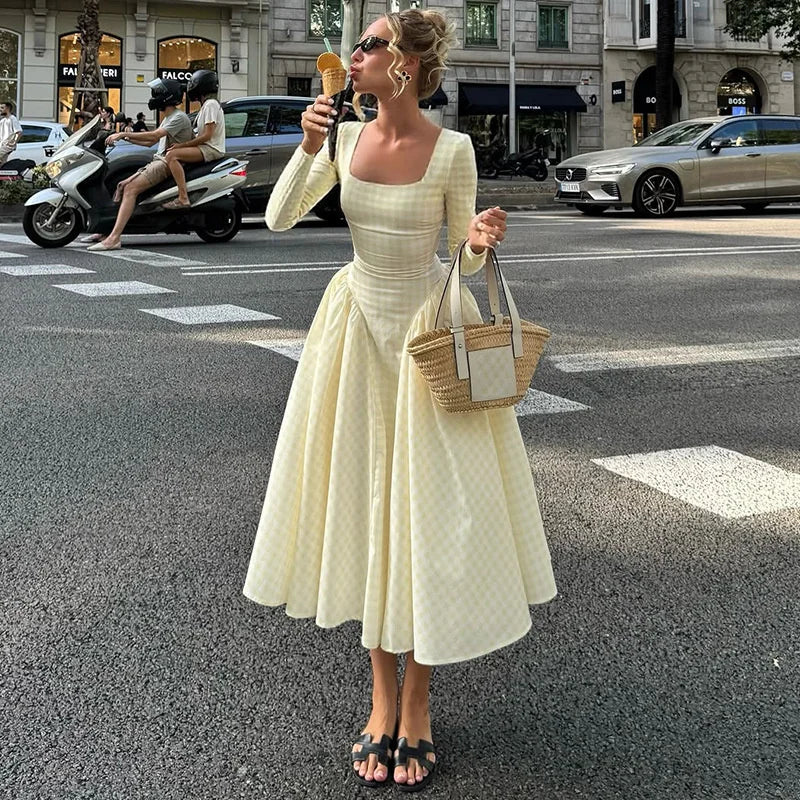 Woman in a white dress holding an ice cream cone and a bag on a city street.