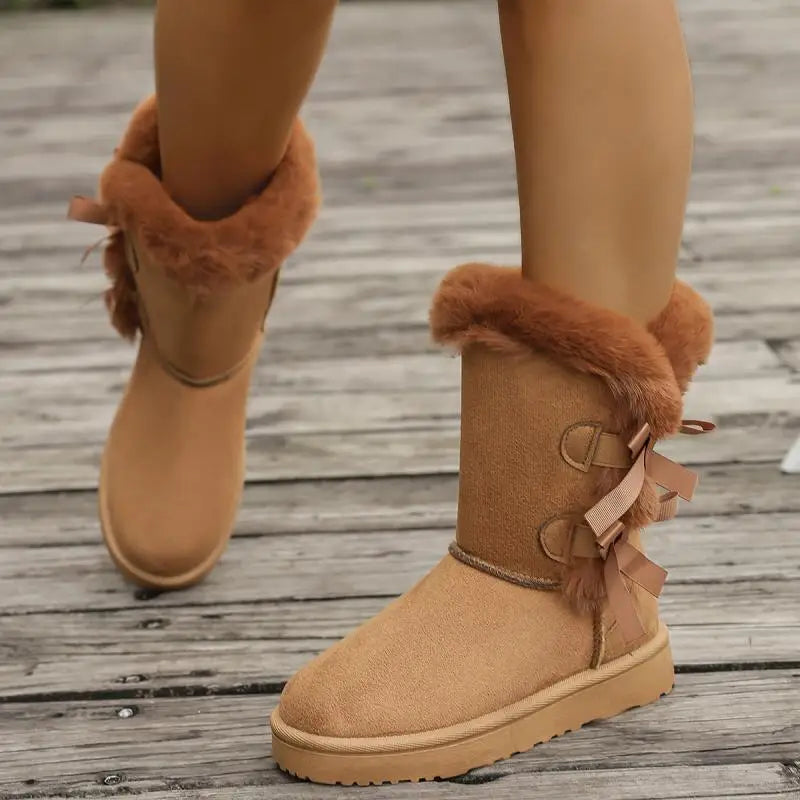 Tan suede boots with fur trim and a bow on a wooden floor.