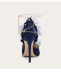 Navy blue high-heeled shoe with floral decorations and gold chain on a white background