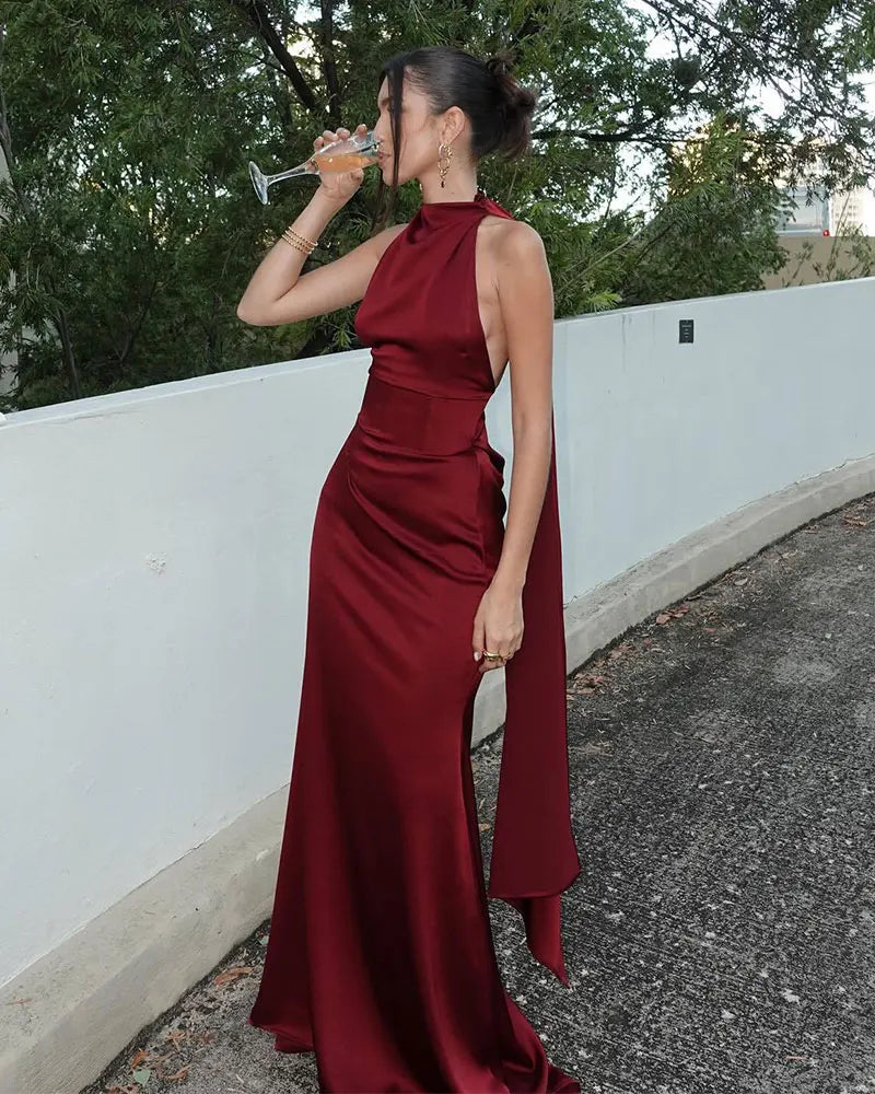 Woman in a burgundy evening gown drinking from a glass outdoors.