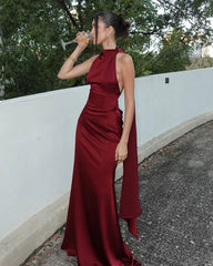 Woman in a burgundy evening gown drinking from a glass outdoors.