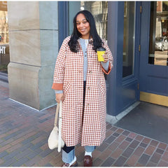 Woman in a checkered coat holding a coffee cup on a city street.