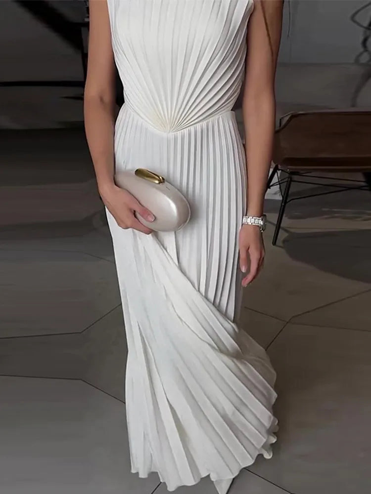 Person wearing a white pleated dress holding a clutch in an indoor setting