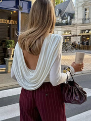 Person wearing a white open-back top and maroon pinstripe pants, holding a coffee cup on a city street.