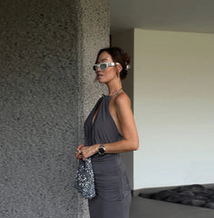 Woman in a gray dress standing against a textured wall.