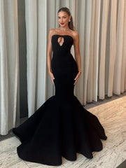 Woman wearing a black strapless gown with a mermaid tail design in front of striped curtains.