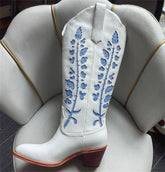 White cowboy boot with blue floral embroidery on a white cushion.