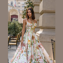 Strappy corset bustier maxi dress with floral motif and green trim, worn by a model sitting at a cafe table.
