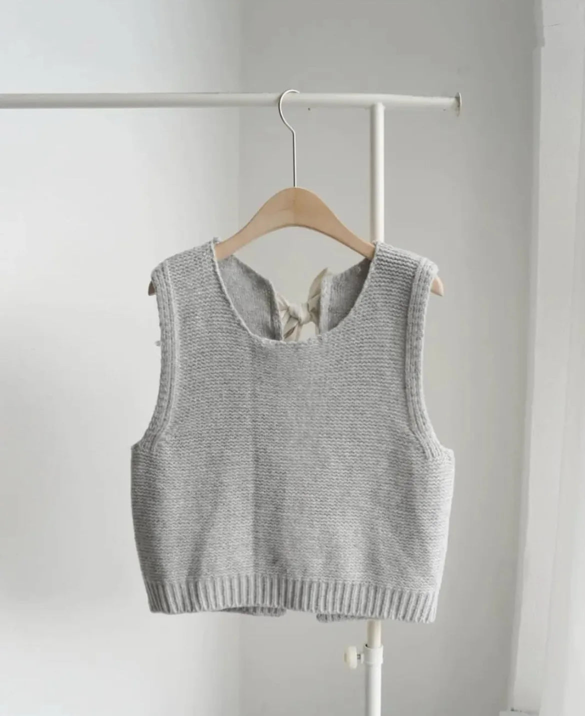 Gray knitted vest on a hanger against a white background