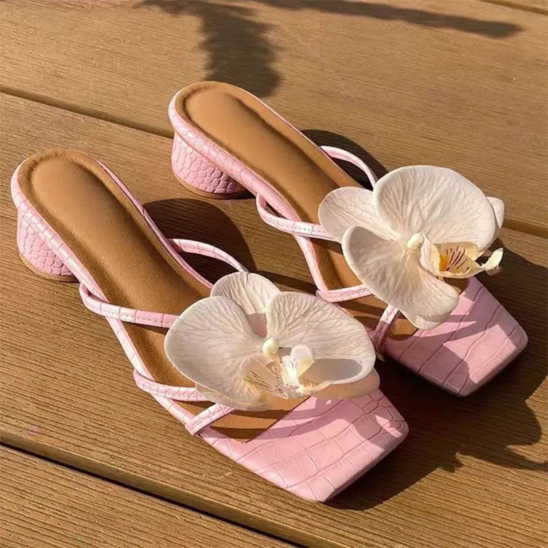 Pink sandals with white floral decorations on a wooden surface