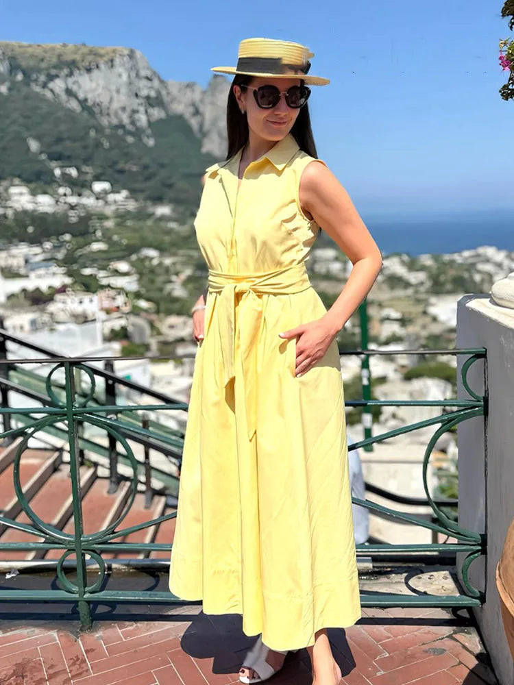 Woman in a yellow dress and hat standing on a balcony with scenic background