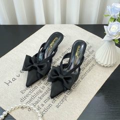Black high-heeled shoes with bow details on a textured surface.