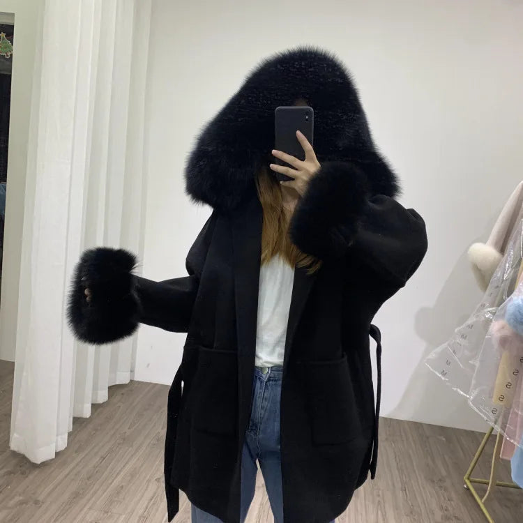 Person wearing a black coat with fur hood in a room.