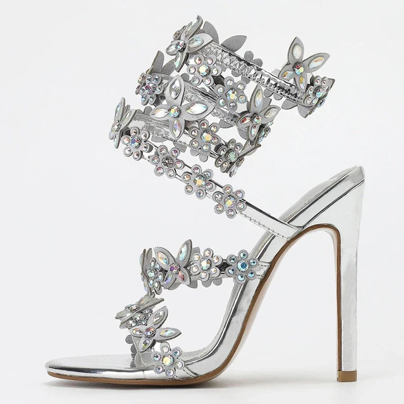 Silver high-heeled sandal with butterfly and flower embellishments on a white background