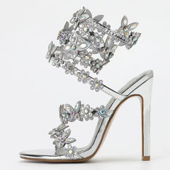 Silver high-heeled sandal with butterfly and flower embellishments on a white background