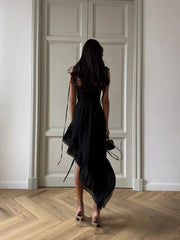 Woman in a black dress standing in a room with wooden flooring and white walls.