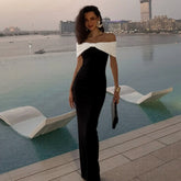 Woman in a black and white dress standing by an infinity pool with a cityscape in the background