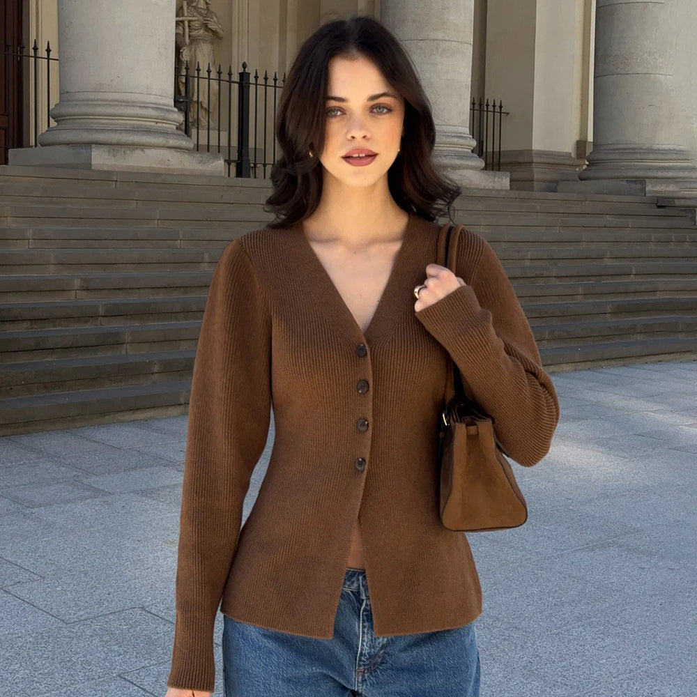 Woman wearing a brown cardigan and blue jeans standing in front of classical architecture.