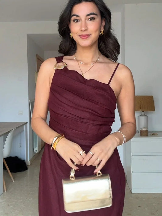 Woman in a burgundy dress holding a gold handbag in a room.
