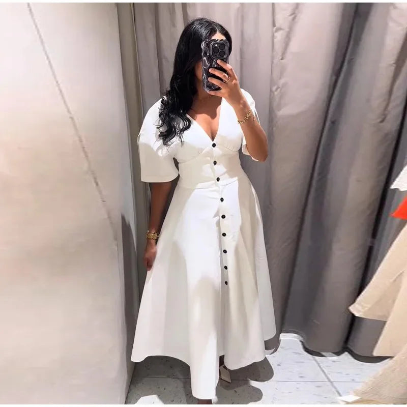 Woman taking a mirror selfie wearing a white dress with black buttons.