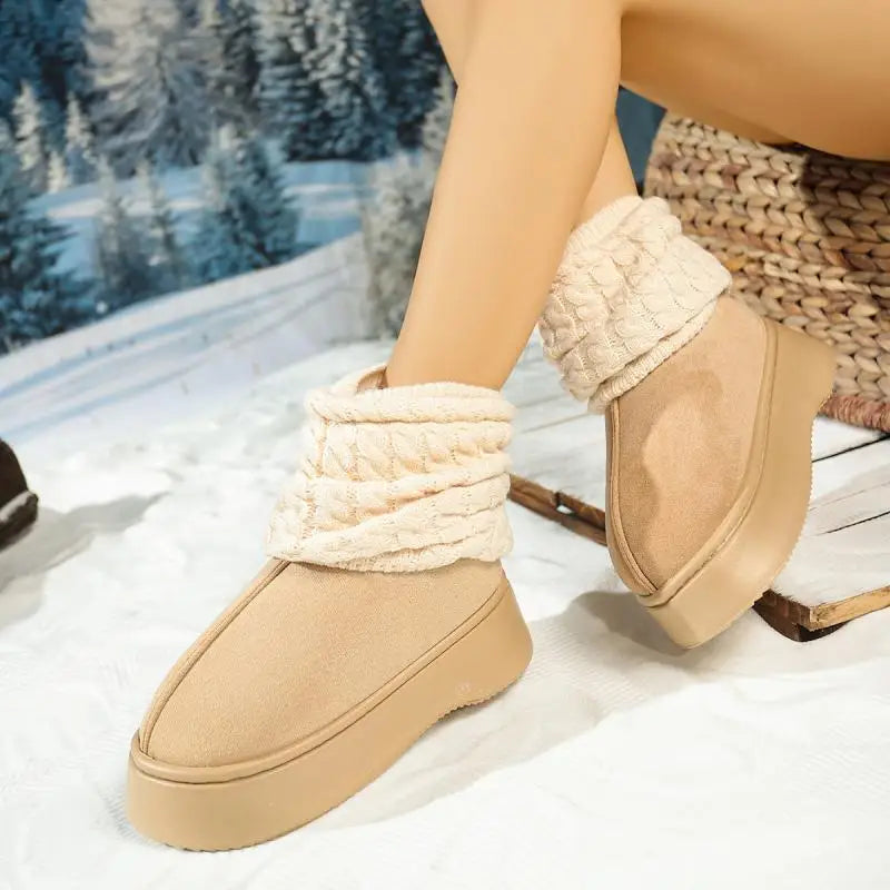 Beige slippers with white fuzzy bands worn by a person sitting on a snowy surface.