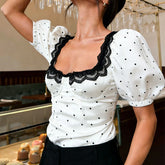 White blouse with black polka dots and lace details worn by a person in an indoor setting.