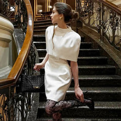 Woman in a white dress standing on a staircase in an elegant interior setting
