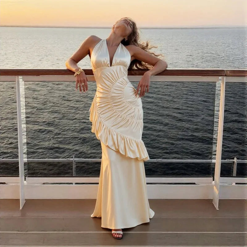 Woman in a white dress standing on a balcony overlooking water at sunset.