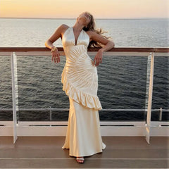 Woman in a white dress standing on a balcony overlooking water at sunset.