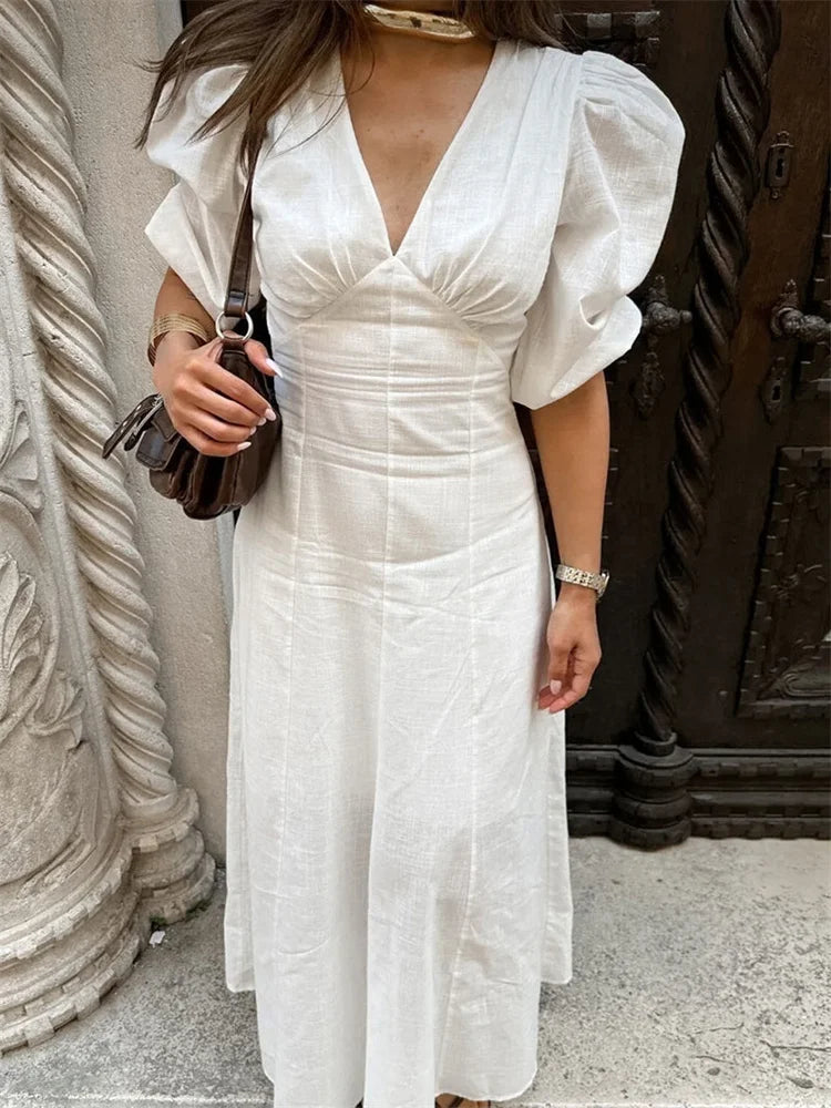 Woman wearing a white dress with puffed sleeves in an indoor setting.