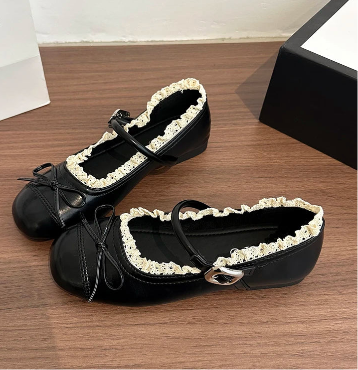 Close-up of a black ballet flat showcasing the round toe, lace trim, and a small bow accent.