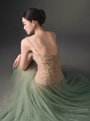 Woman in a elegant dress with a gradient from beige to green, sitting against a dark background.