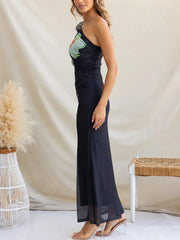 Woman wearing a long, dark blue dress with floral patterns against a neutral background.