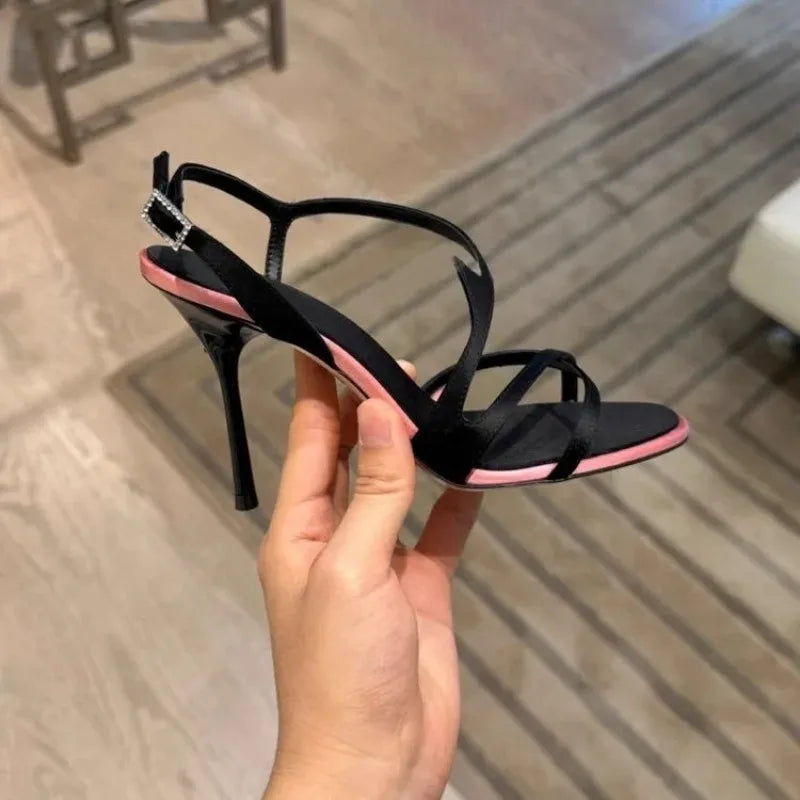Hand holding a black stiletto strap sandal with pink trim