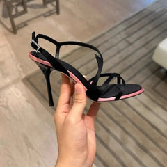 Hand holding a black stiletto strap sandal with pink trim