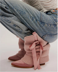 Close-up of ribbed knit slouchy boots with satin pointed toe and bow accent on a person's legs.