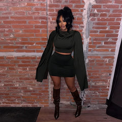 Person wearing a black outfit with a long coat against a brick wall.