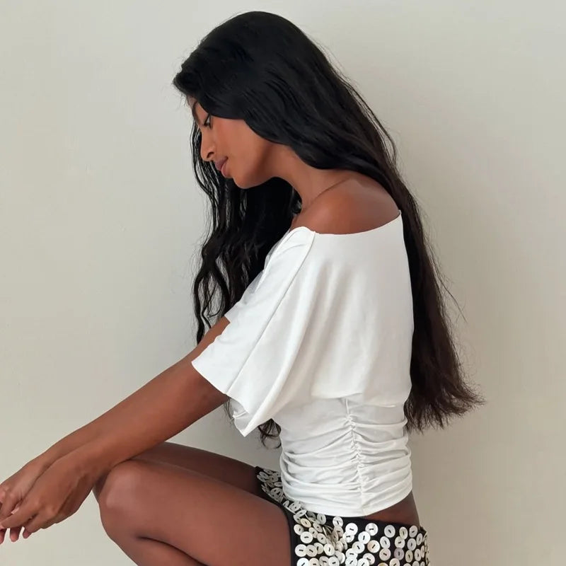 Woman wearing a white off-shoulder top and patterned pants against a plain background