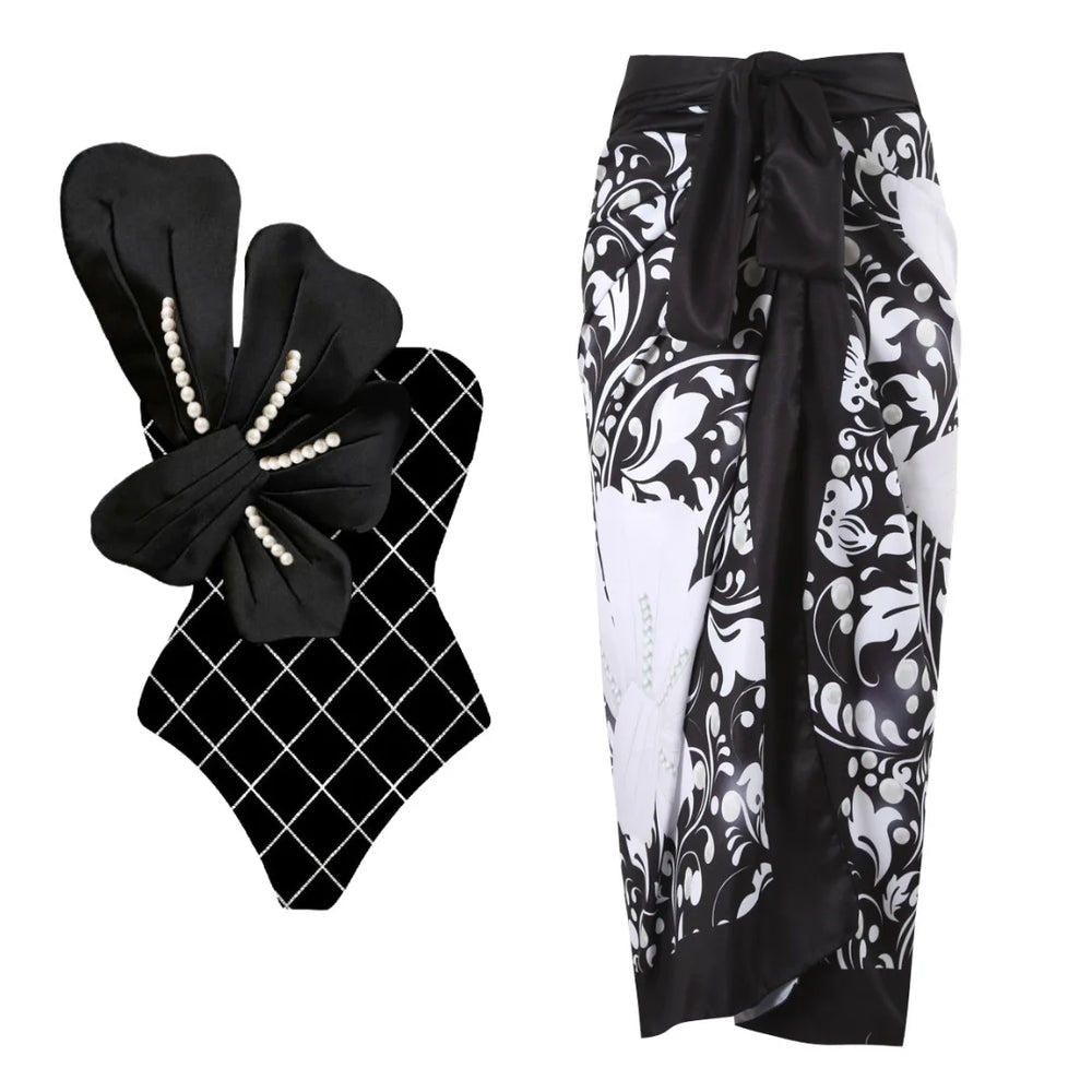 Black and white one-piece swimsuit with white floral embellishment and pearl details, paired with a black and white floral wrap skirt.