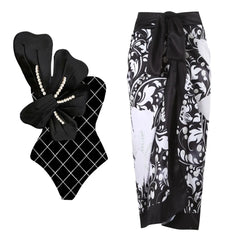 Black and white one-piece swimsuit with white floral embellishment and pearl details, paired with a black and white floral wrap skirt.