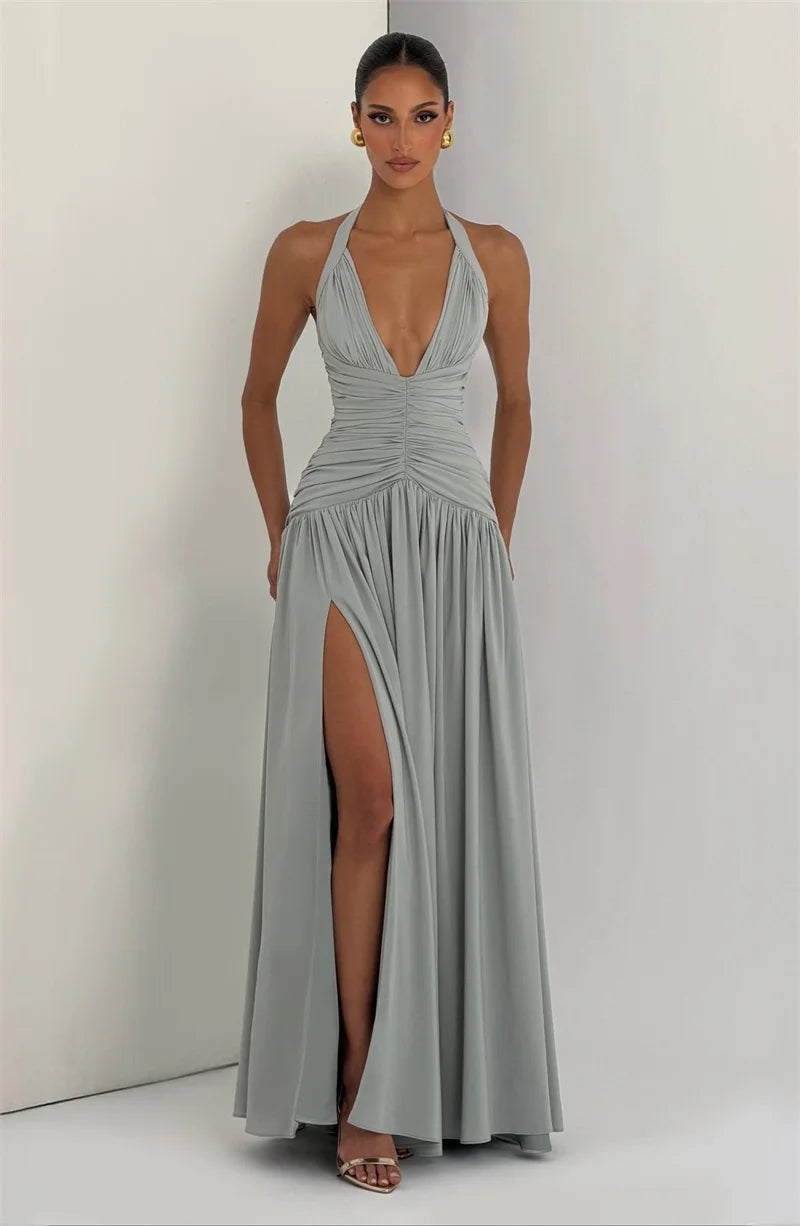 Woman wearing a silver halter neck gown with a high slit on a plain background