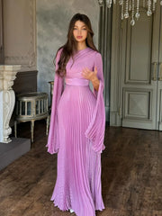 Woman in a pink pleated dress standing in an elegant room with decorative elements.