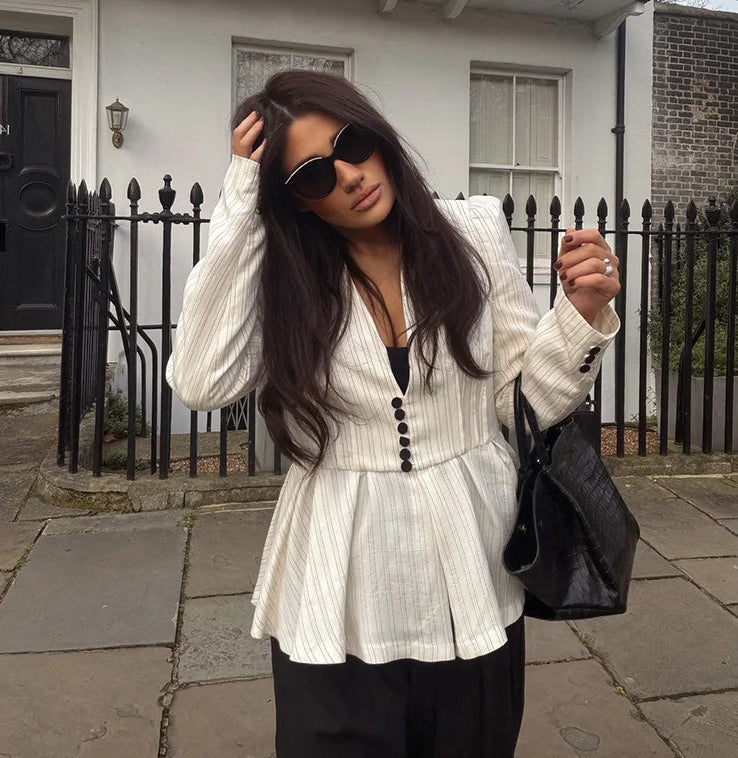 Woman in a white blazer with black buttons standing on a sidewalk.