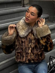 Person wearing a leopard print fur coat sitting on steps.