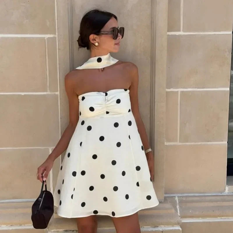 Woman wearing a white dress with black polka dots against a beige wall.