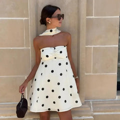Woman wearing a white dress with black polka dots against a beige wall.