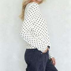 Person wearing a white blouse with black polka dots and dark jeans against a light background