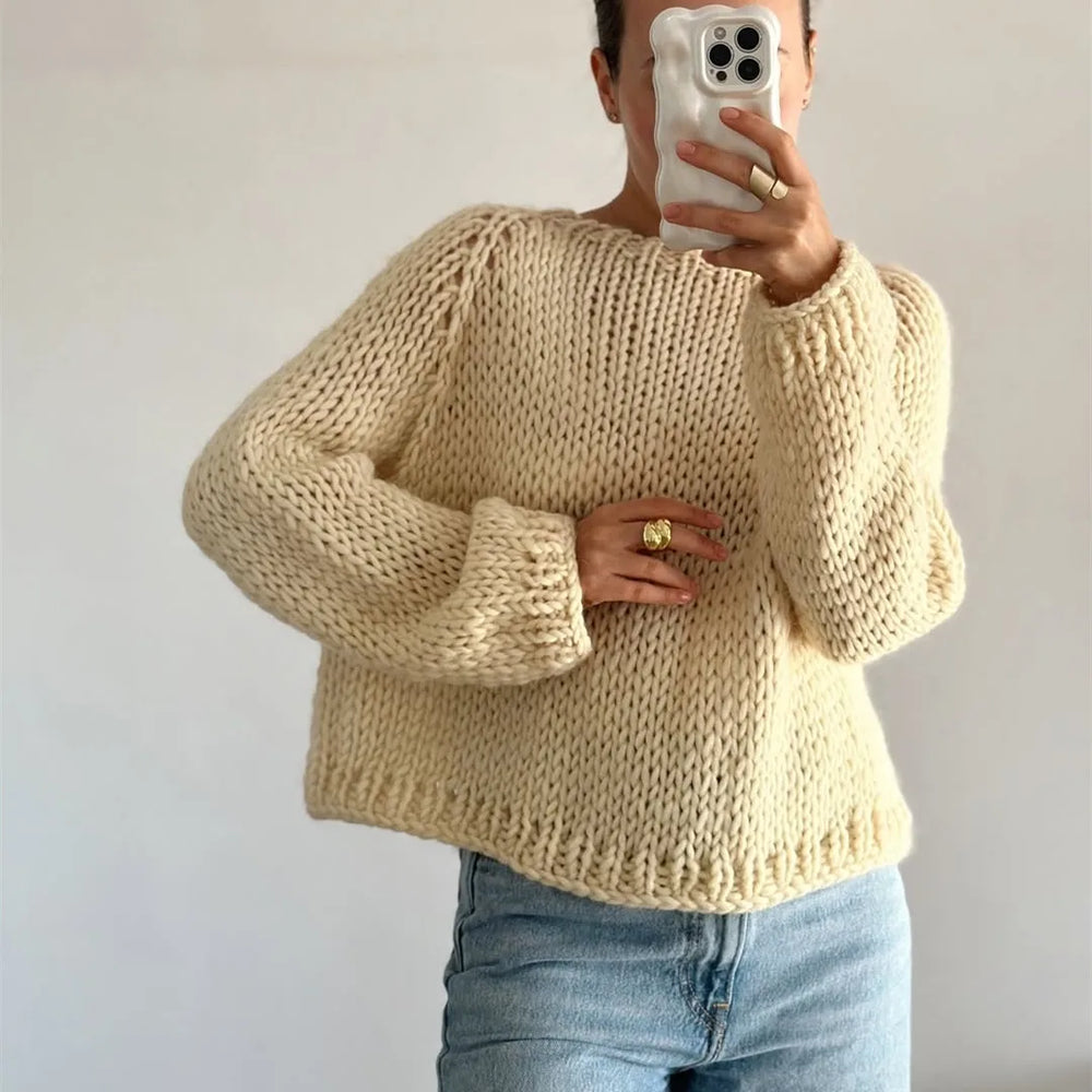 Person wearing a beige knitted sweater and blue jeans, taking a mirror selfie.