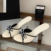 White heeled mules with black trim and a black bow